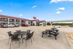 Un motel con asientos al aire libre, un letrero rojo y un estacionamiento lleno de coches.