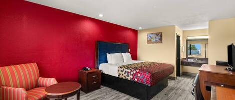 Una habitación de hotel con pared roja, una cama con colcha estampada, un sofá a rayas, una pequeña mesa de madera y un escritorio con televisor.