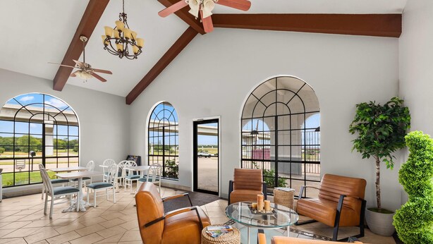 A spacious indoor area with large arched windows, leather seating, a glass table, and a ceiling fan.