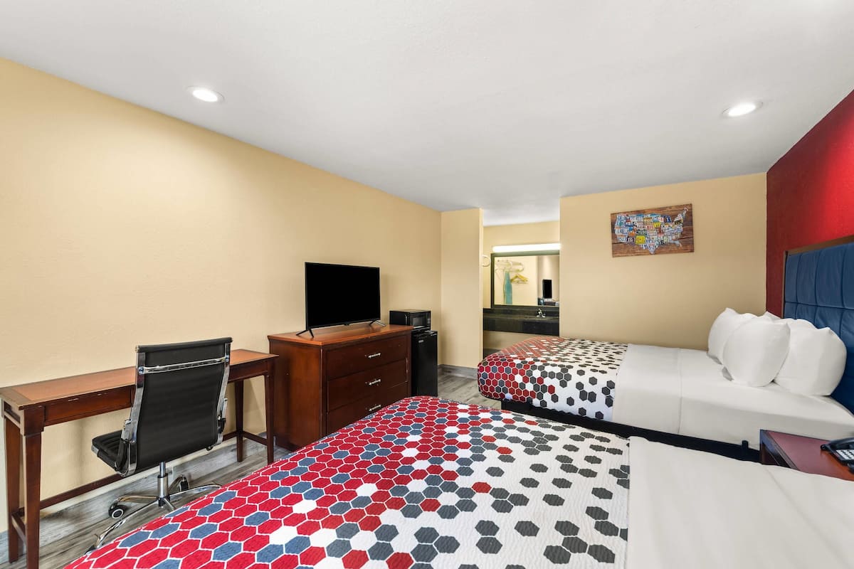 Quarto de hotel com duas camas, uma escrivaninha, uma cadeira, uma televisão e uma cômoda.