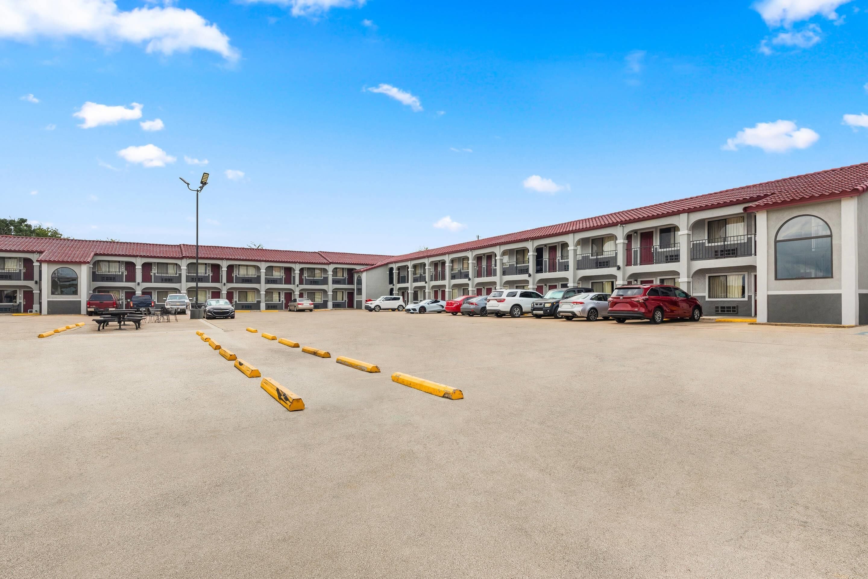 A motel with multiple floors, a parking lot with yellow bollards, and several cars parked.