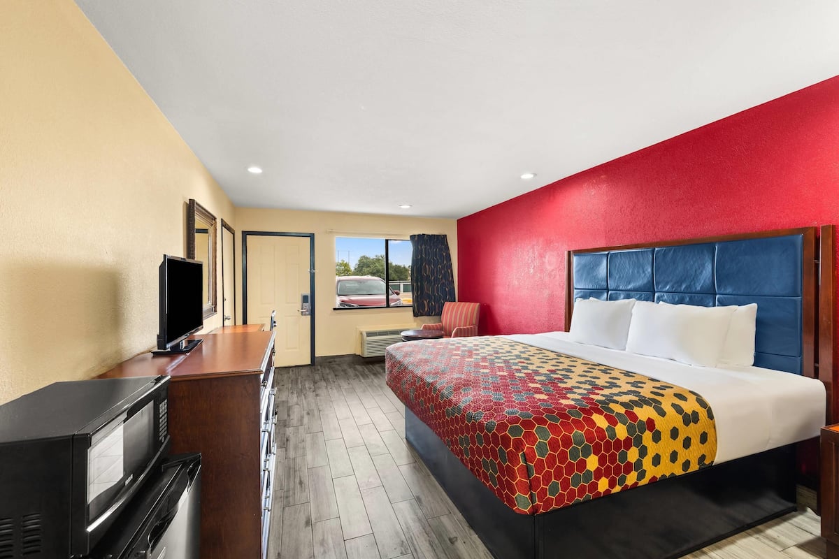 Quarto de hotel com cama, televisão, escrivaninha e janela.