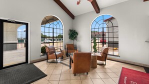 A spacious lobby with arched windows, comfortable seating, a ceiling fan, and a view of the parking area.