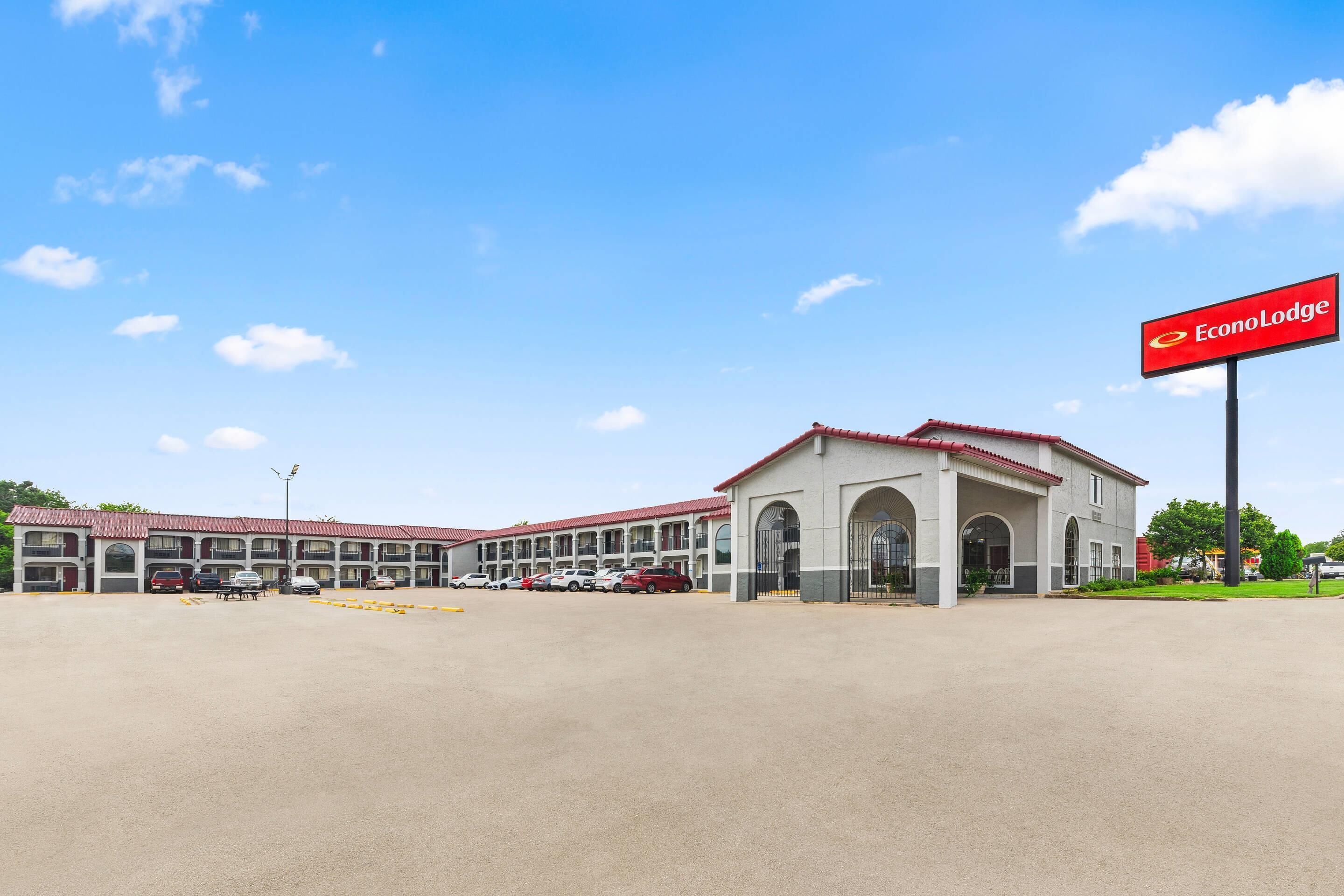 A hotel with a red and white facade, multiple parking spaces, and a clear blue sky.