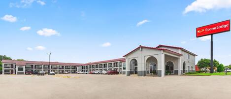 A hotel with a red and white facade, multiple parking spaces, and a clear blue sky.