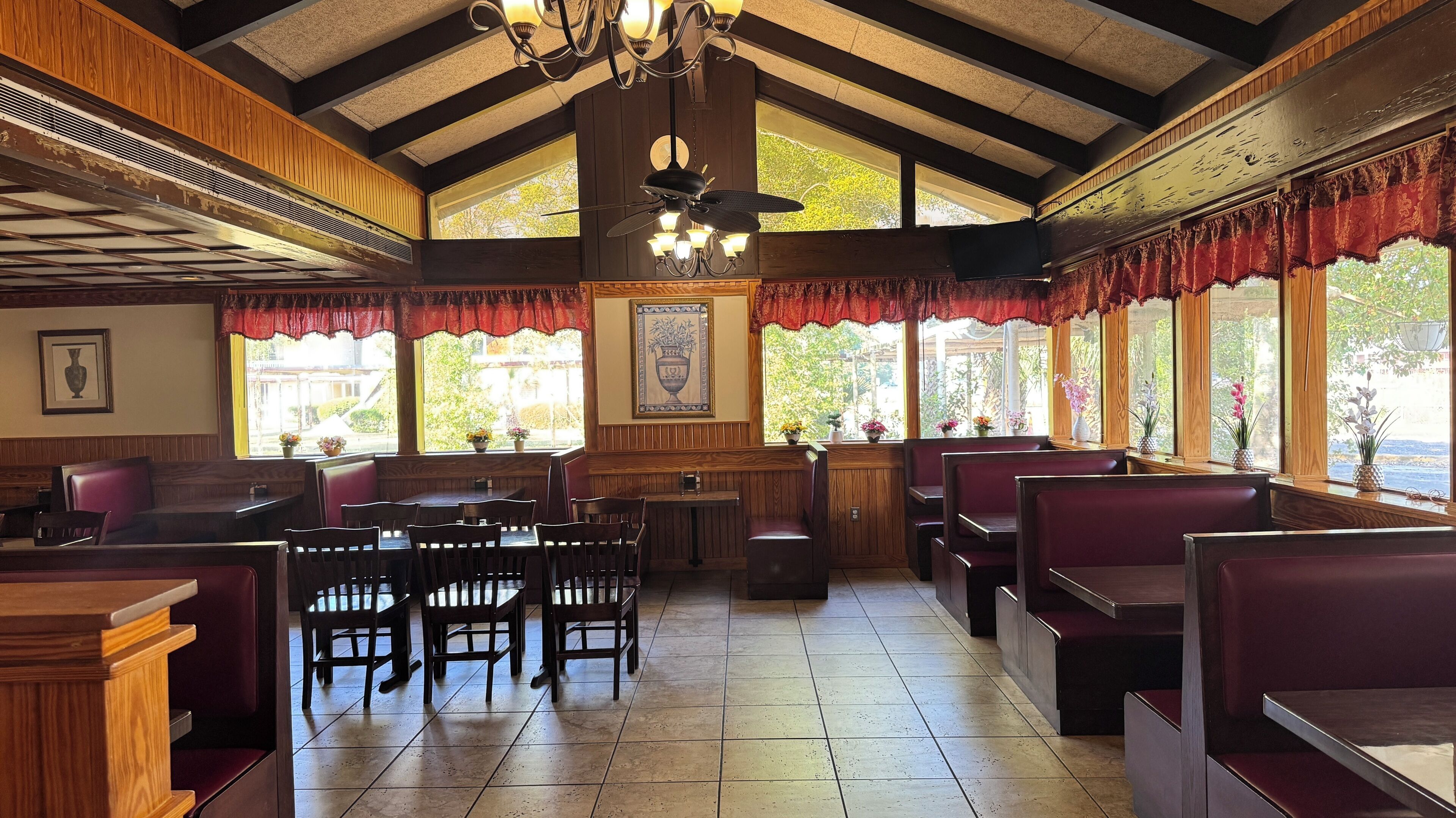 A restaurant interior with wooden paneling, red upholstered booths, and a chandelier.