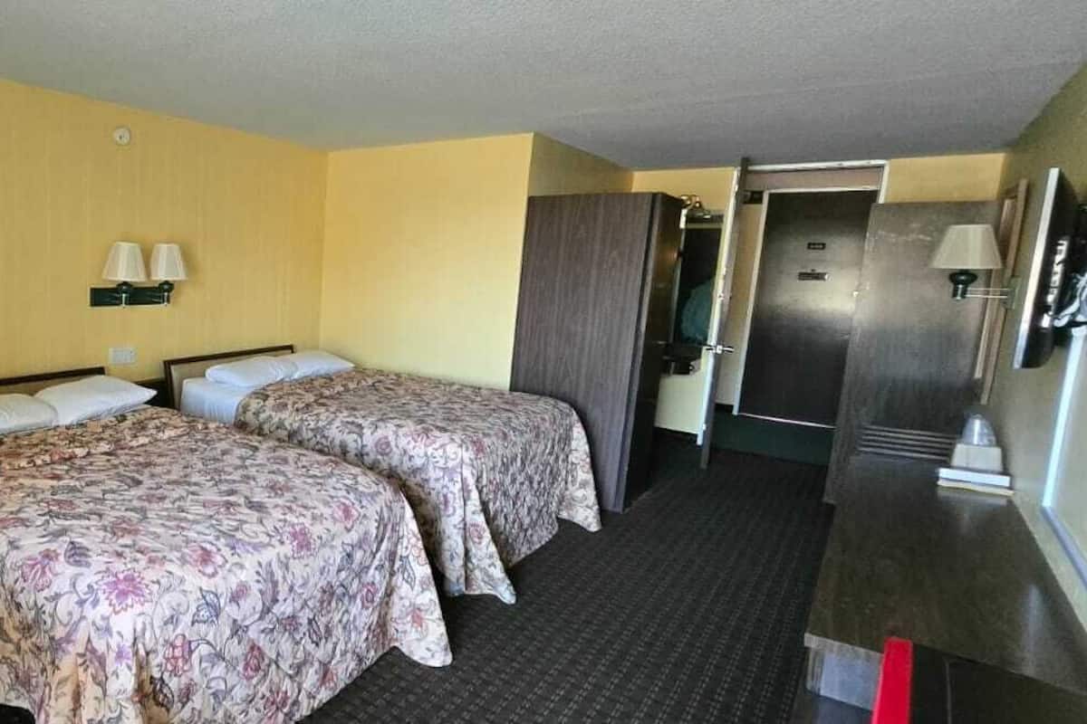 Habitación de hotel con dos camas, un escritorio, una silla, un armario y un baño.