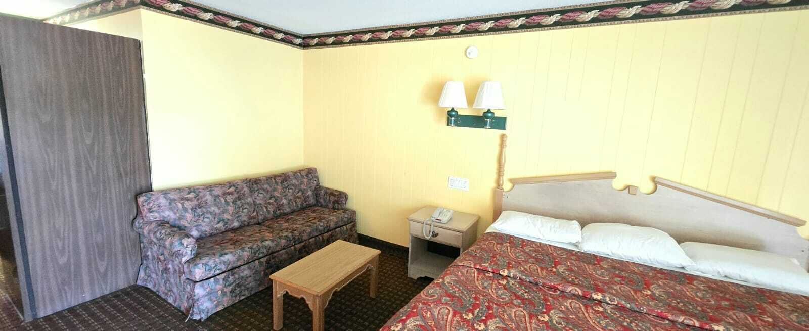 Una habitación de hotel con una cama, un sofá, una mesita de noche y una lámpara.