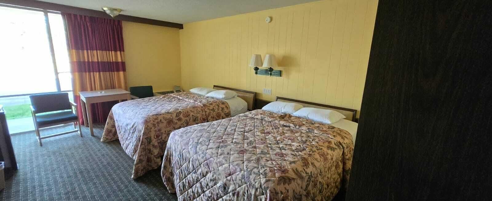 A hotel room with two beds, a desk, a chair, and a window with curtains.