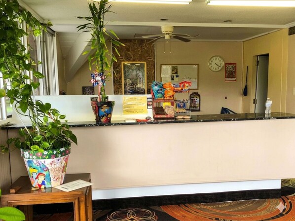 Una zona de recepción con mostrador, reloj, ventilador de techo y planta en maceta.