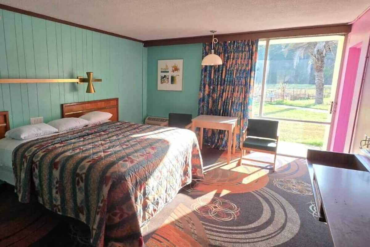 Un dormitorio con cama, escritorio, silla, ventana con cortinas y vistas al exterior.