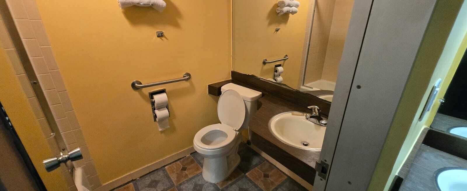 Un baño pequeño con inodoro, lavamanos y barras de apoyo.