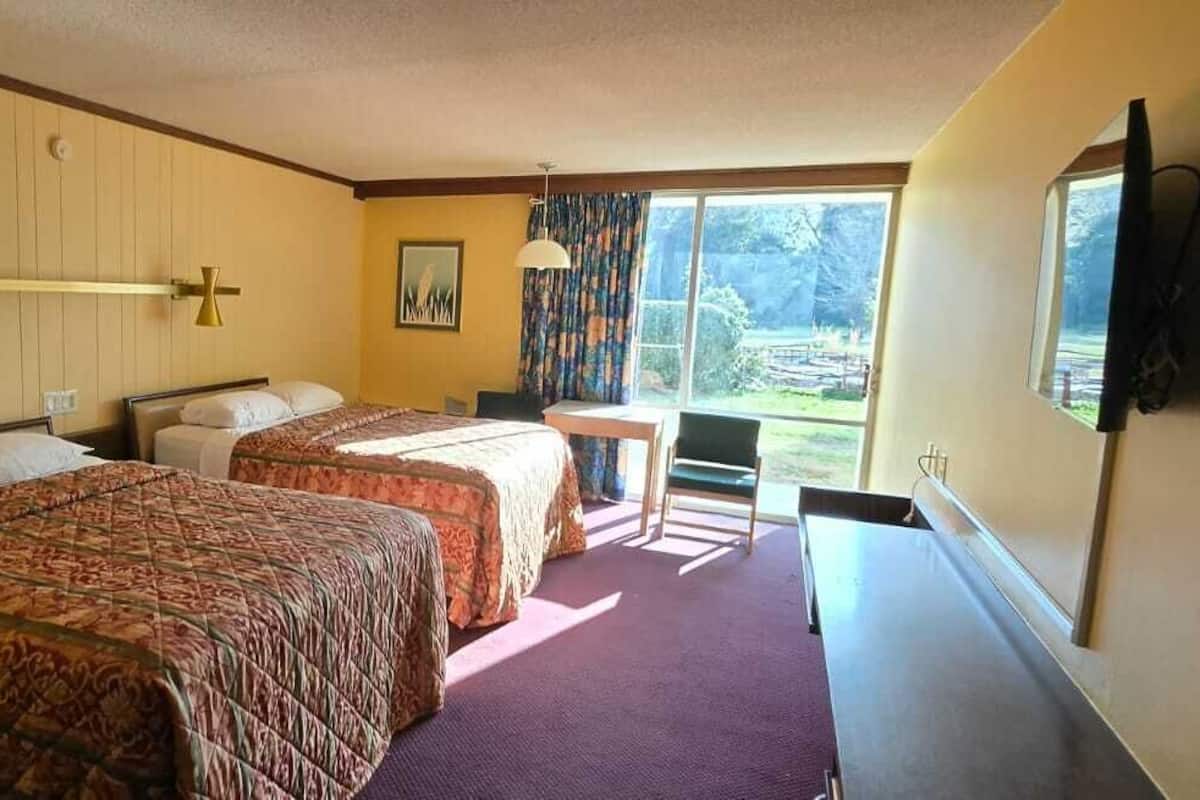 Habitación de hotel con dos camas, un escritorio, una silla, un televisor y un ventanal grande.