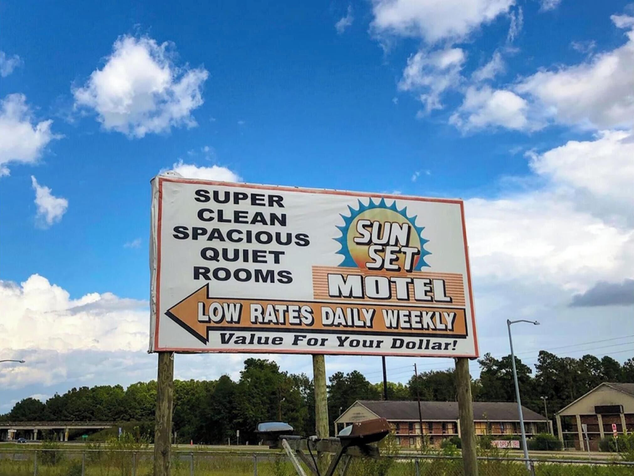 A motel sign advertising 'Super Clean Spacious Quiet Rooms' with a sunburst logo and 'Low Rates Daily Weekly' text.