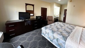 A hotel room with a bed, a TV, a desk with a chair, a microwave, and a mirror.