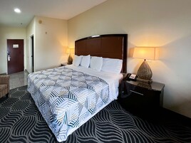Quarto de hotel com uma cama grande, uma mesa de cabeceira com abajur e um tapete estampado com padrão de zebra.