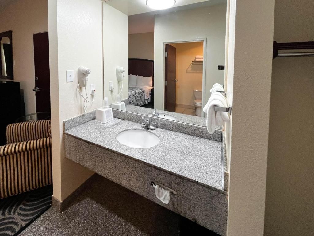 A hotel bathroom with a granite countertop sink, a mirror, a hairdryer, and a towel rack.
