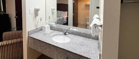 A hotel bathroom with a granite countertop sink, a mirror, a hairdryer, and a towel rack.