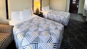 A hotel room with two beds, a nightstand with a lamp, a striped sofa, and a patterned carpet.
