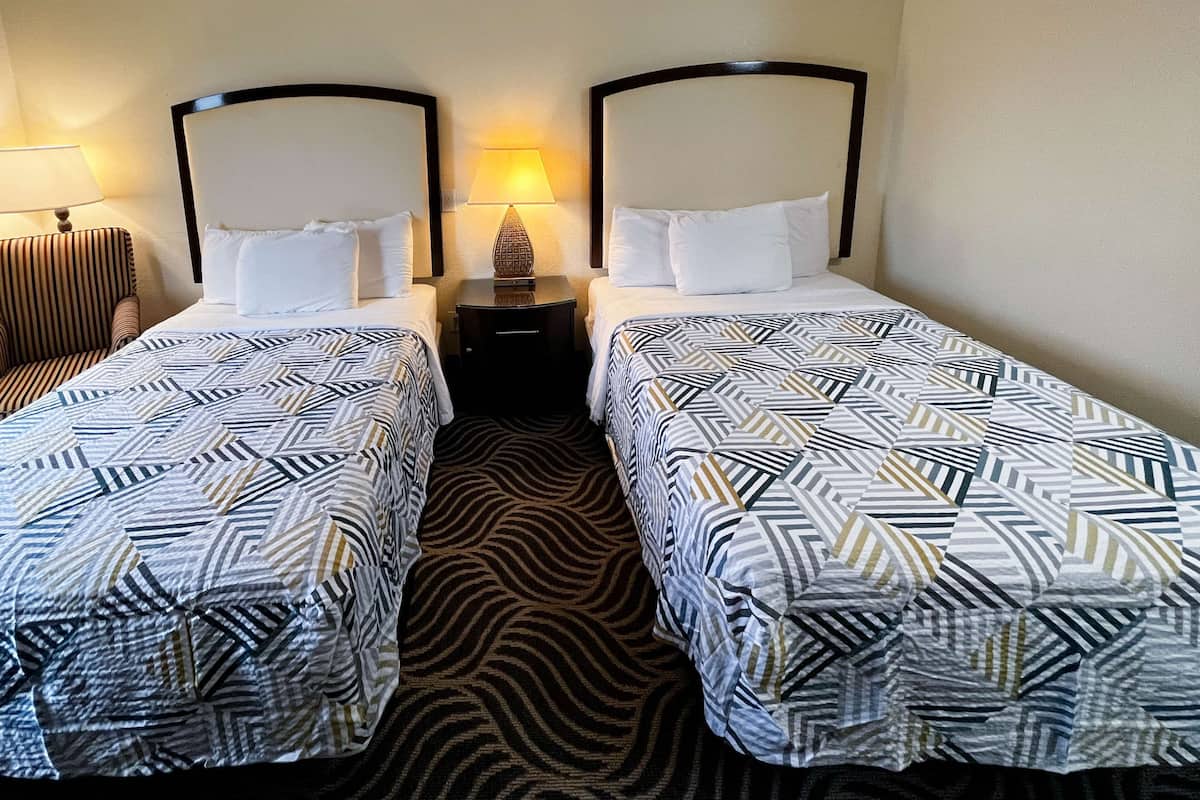 Ett hotellrum med två separata sängar, var och en med ett mönstrat överkast, ett nattduksbord med en lampa och en matta med zebrasträck.