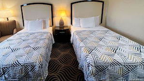 A hotel room with two single beds, each with a patterned bedspread, a nightstand with a lamp, and a zebra-patterned carpet.