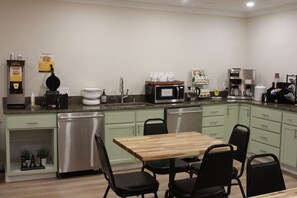 A compact kitchen with a wooden table, black chairs, a stainless steel refrigerator, a microwave, and a coffee machine. - Boulder Twin Lakes Inn (Boulder)