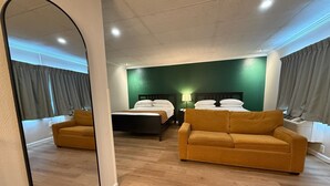 Habitación de hotel con dos camas, un sofá, un espejo e iluminación empotrada en el techo.