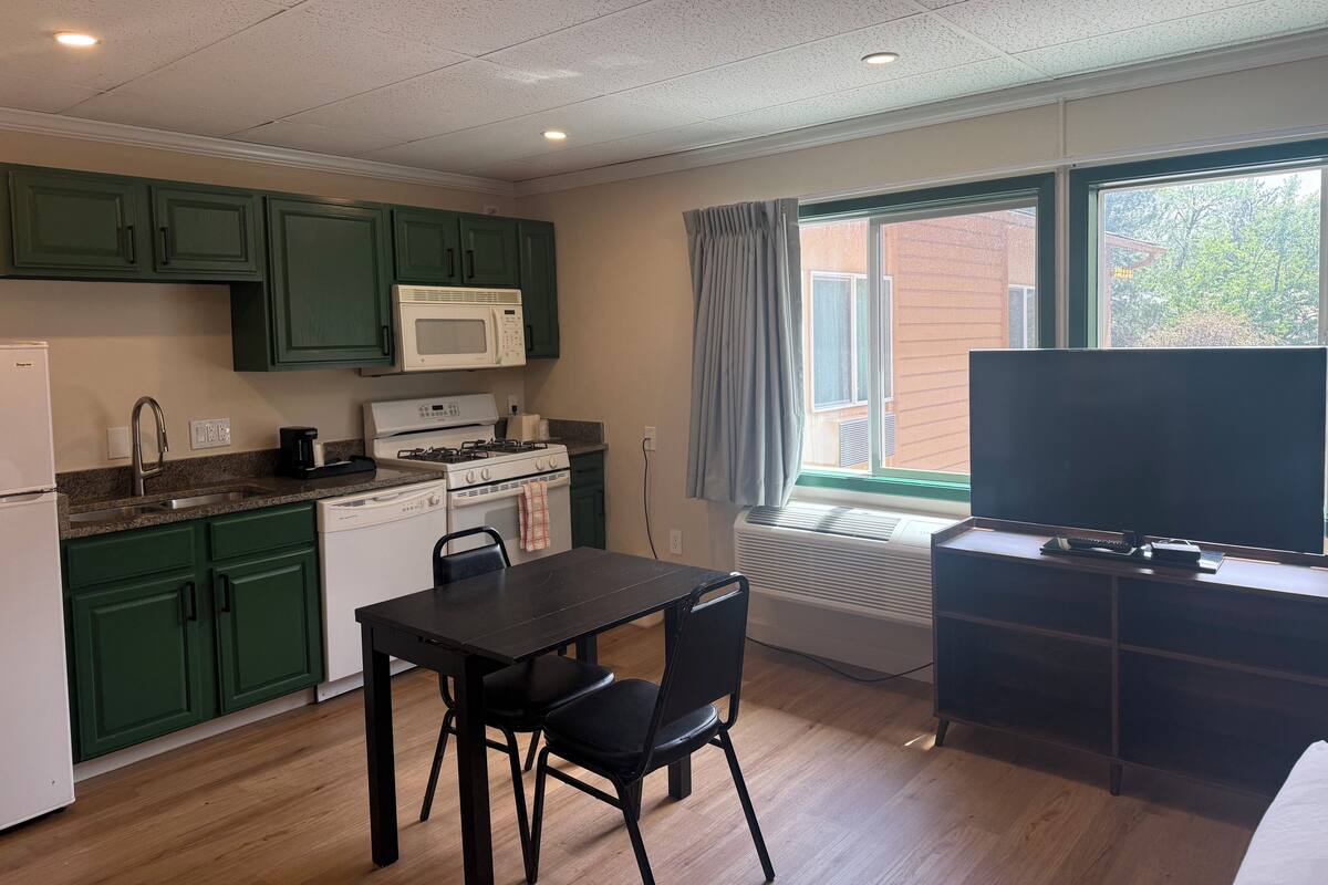 A compact kitchen with green cabinets, a microwave, stove, and a dining table with chairs.