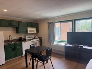 A compact kitchen with green cabinets, a microwave, stove, and a dining table with chairs.