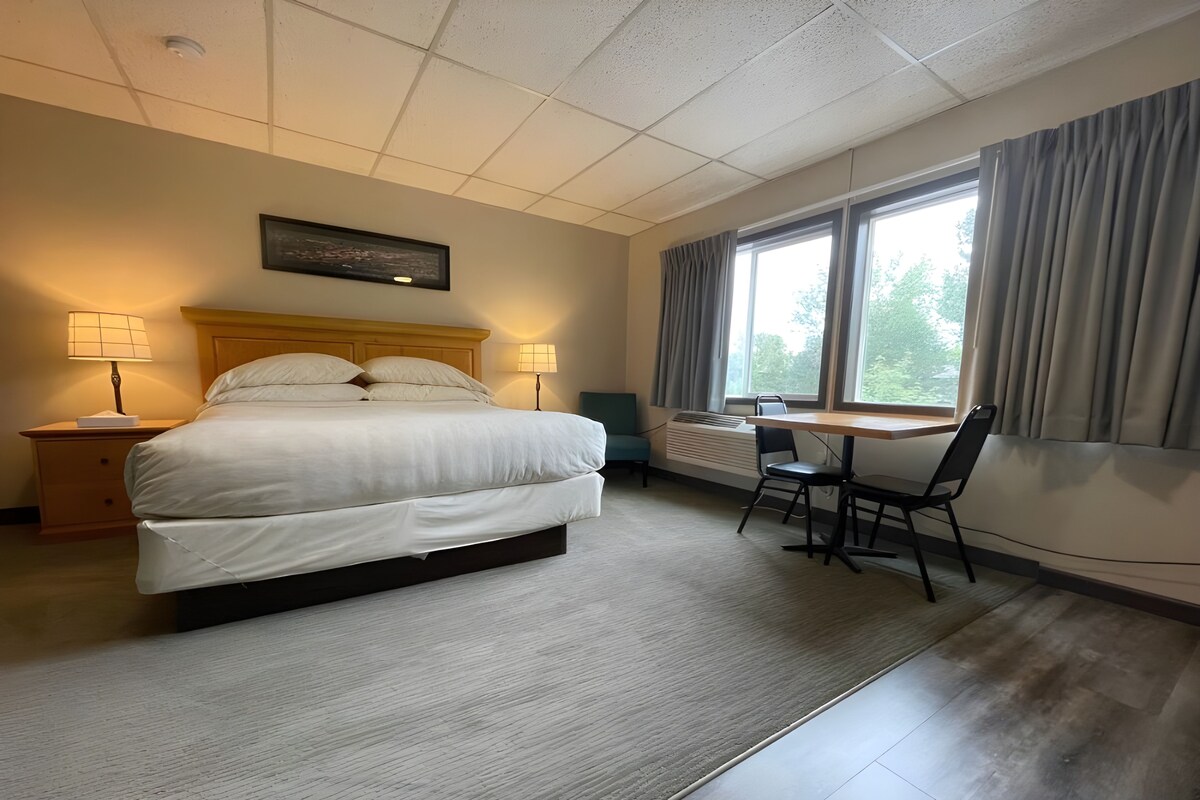 A hotel room with a bed, bedside lamps, a desk, and a chair.