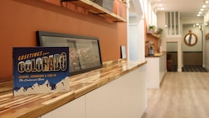 Un mostrador de recepción con un cuadro enmarcado, un libro titulado 'Greetings from Colorado' y una estantería con plantas.