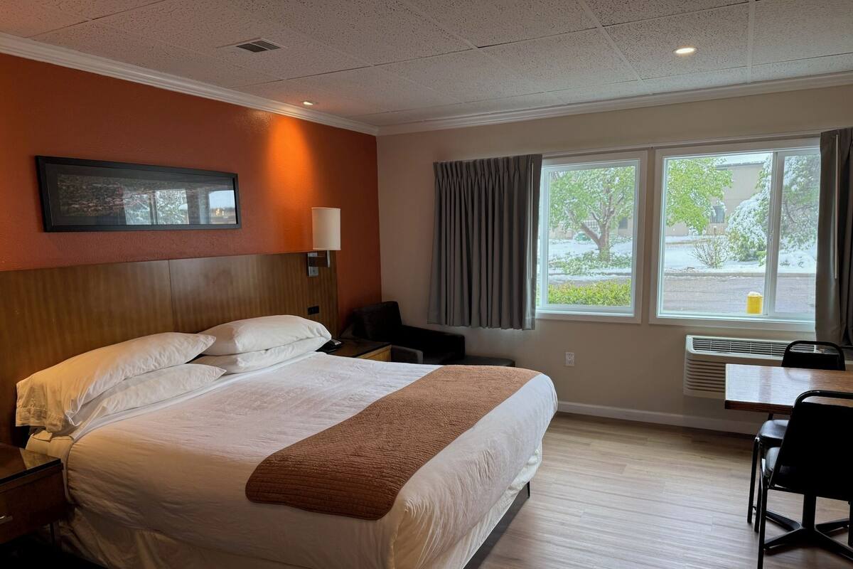 A hotel room with a bed, bedside table, lamp, window with curtains, and a view of the outside.