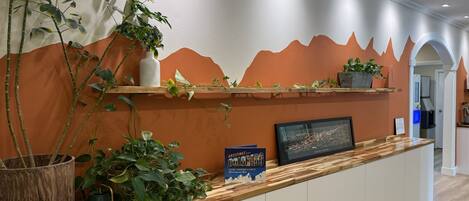 A reception desk with a wooden counter, potted plants, a framed picture, and a book titled 'GREATFUL'.