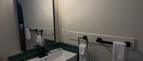 A bathroom with a white sink, a mirror with a black frame, and a towel rack with white towels.