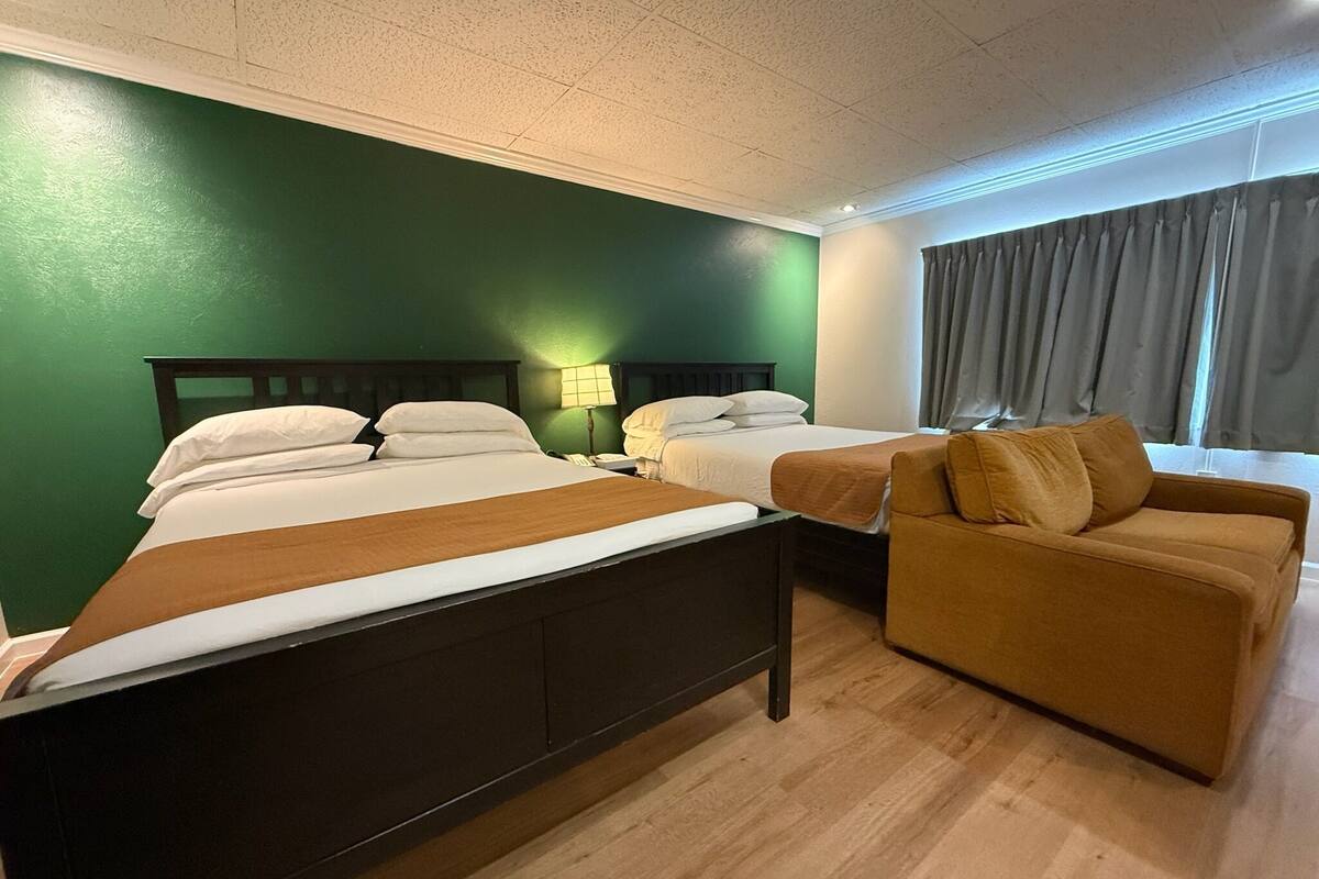 A hotel room with two beds, a sofa, a lamp, and a window with curtains.