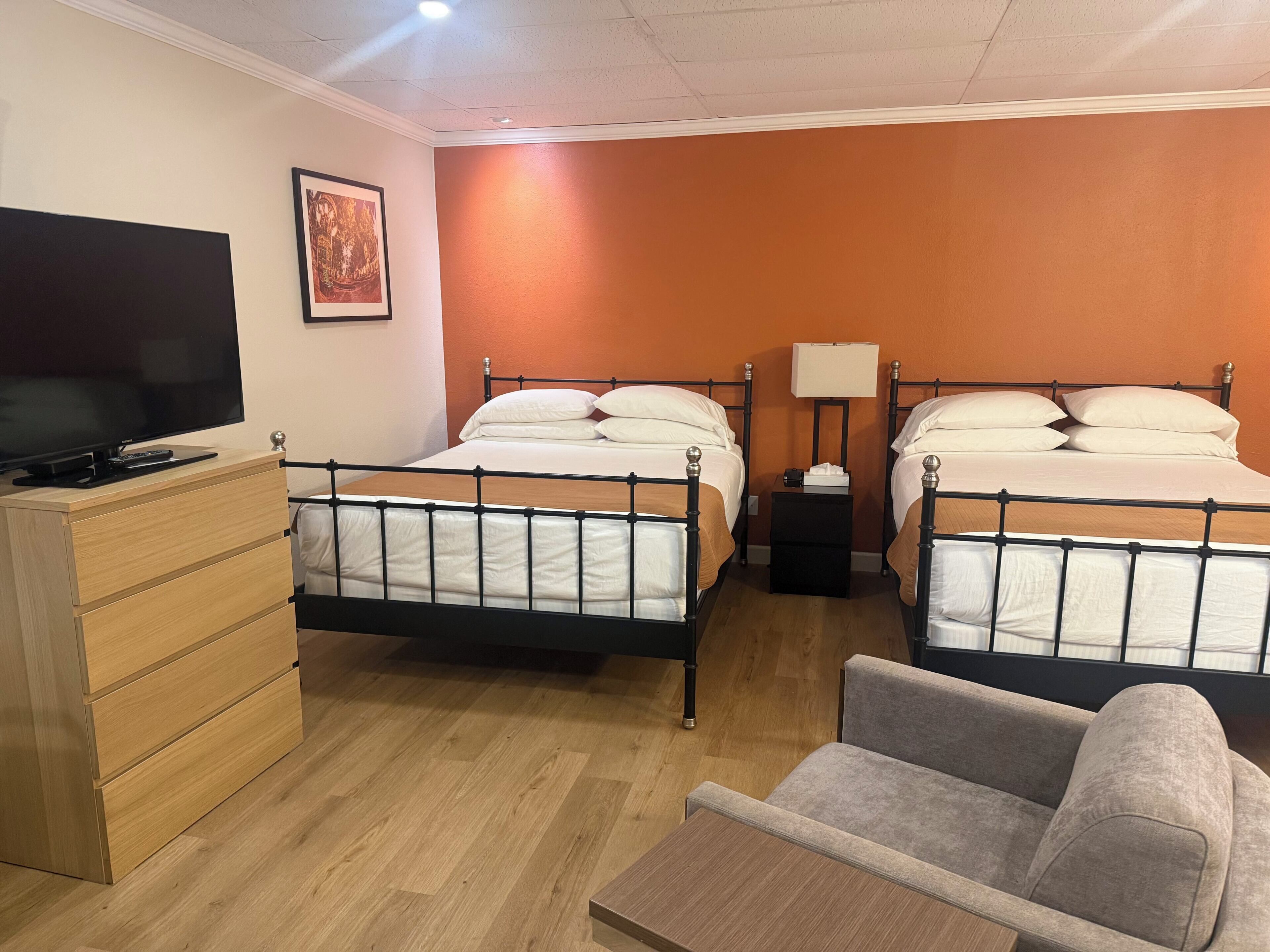 A hotel room with two beds, a TV, a dresser, and a sofa.