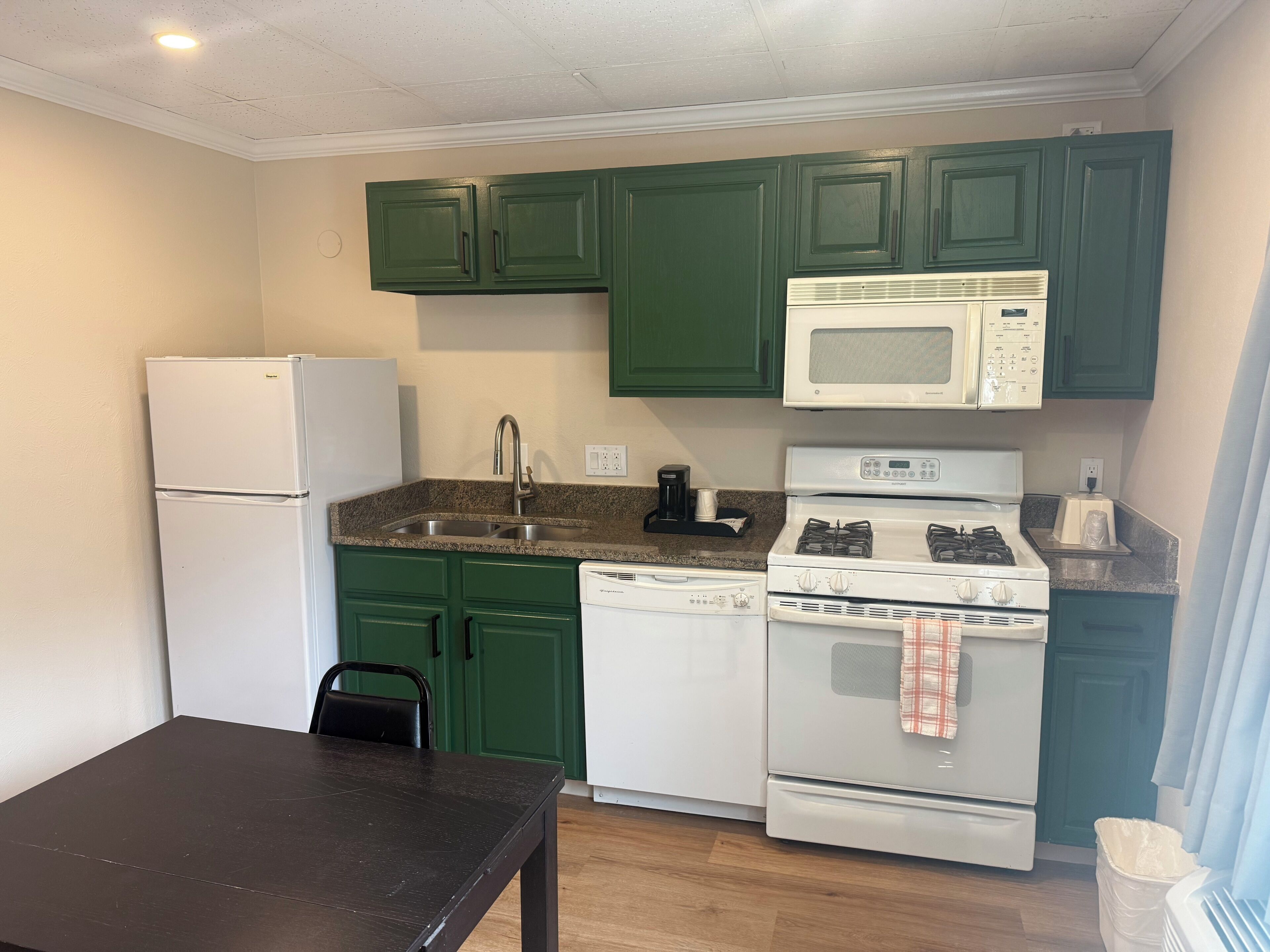 A compact kitchen with green cabinets, a white refrigerator, a microwave, a stove, and a sink.