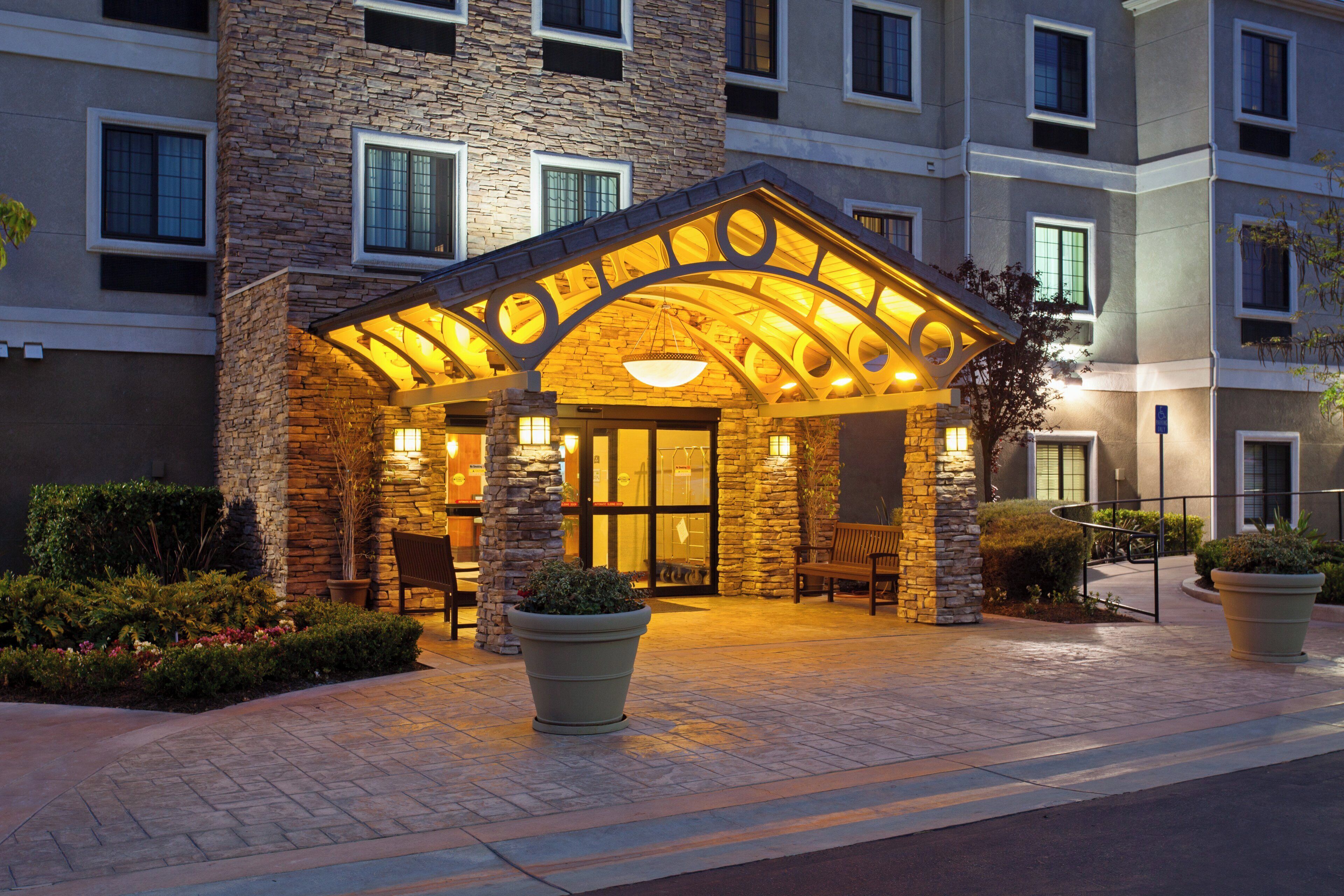 Fachada de hotel de piedra, con un patio cubierto y mobiliario de exterior.