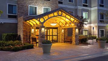 A hotel entrance with a stone facade, a covered patio area, and outdoor seating.