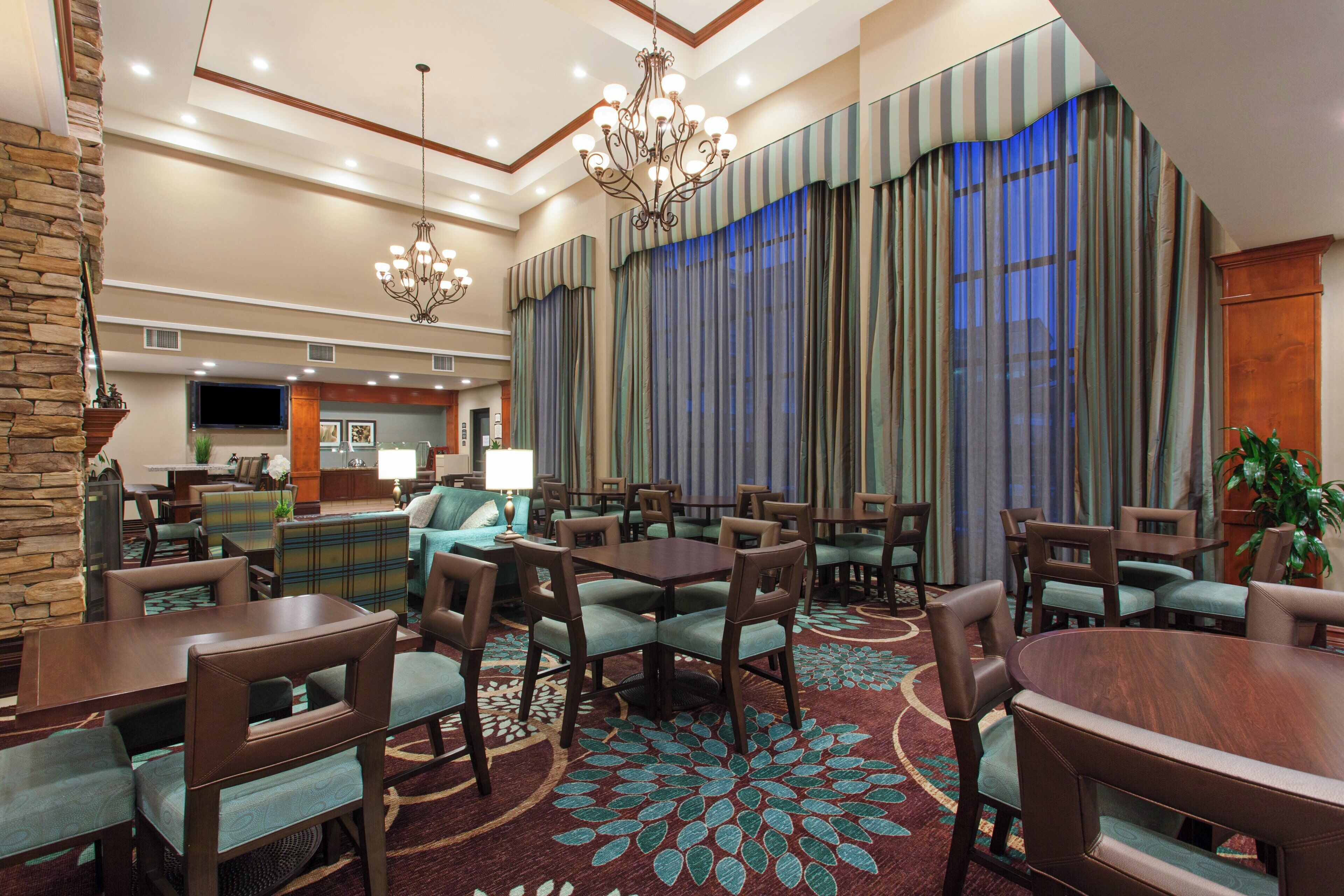 Um saguão de hotel com área de refeições, cozinha e uma grande janela com cortinas.