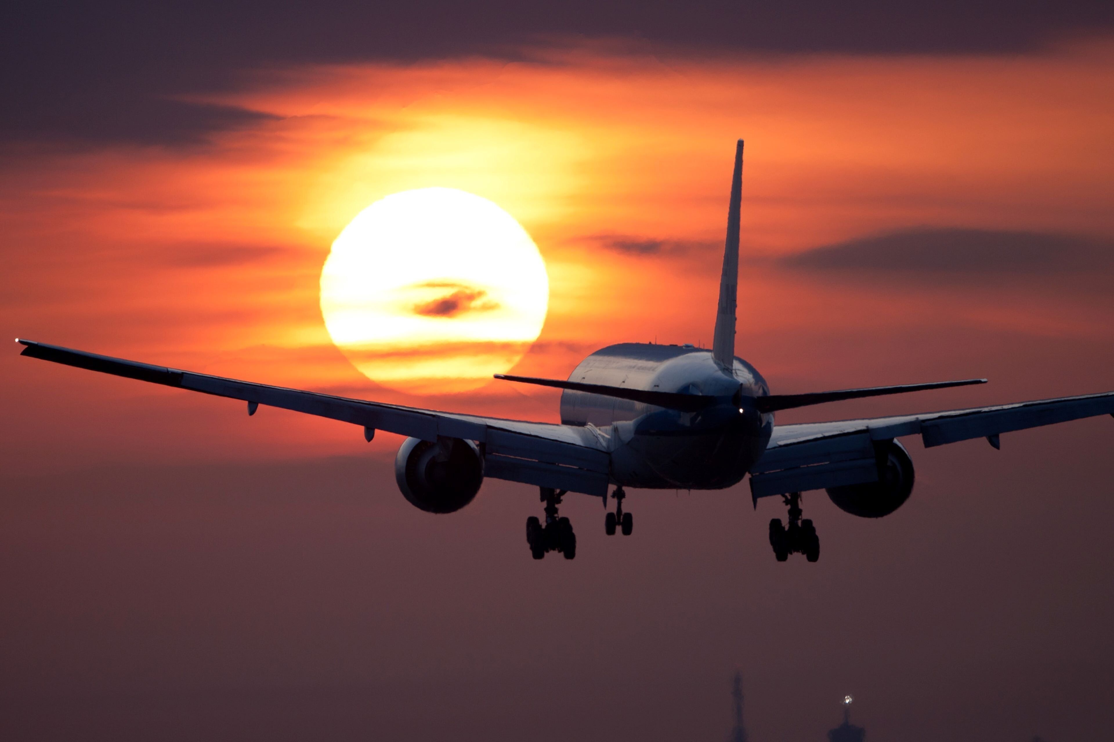 An airplane flying with a sunset in the background.
