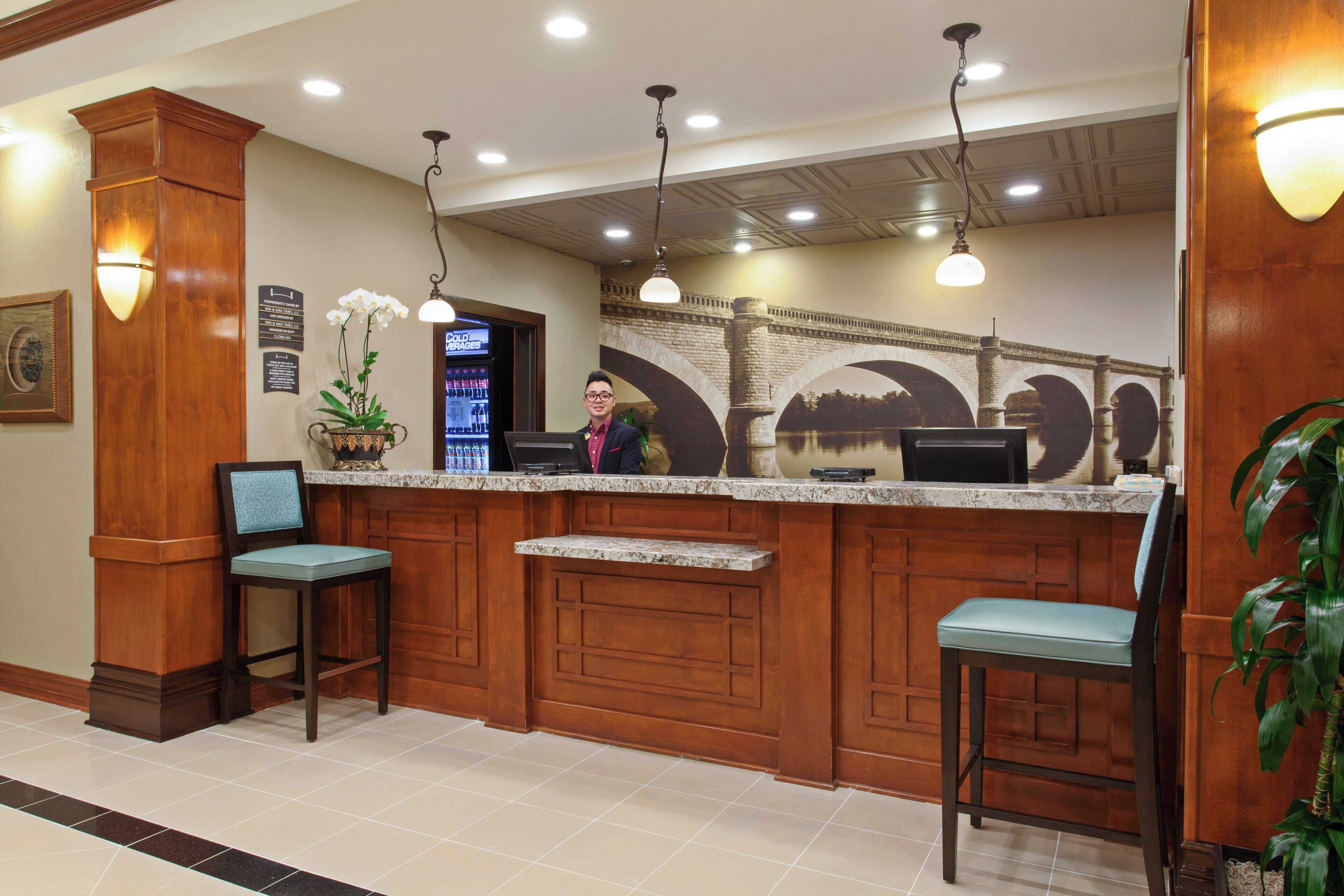 A reception area with a marble counter, two bar stools, a potted plant, and a wall-mounted sign.