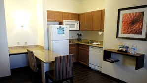 A compact kitchen with wooden cabinets, a refrigerator, a microwave, a sink, and a dining area with striped chairs. - Staybridge Suites Lake Forest by IHG (Foothill Ranch)