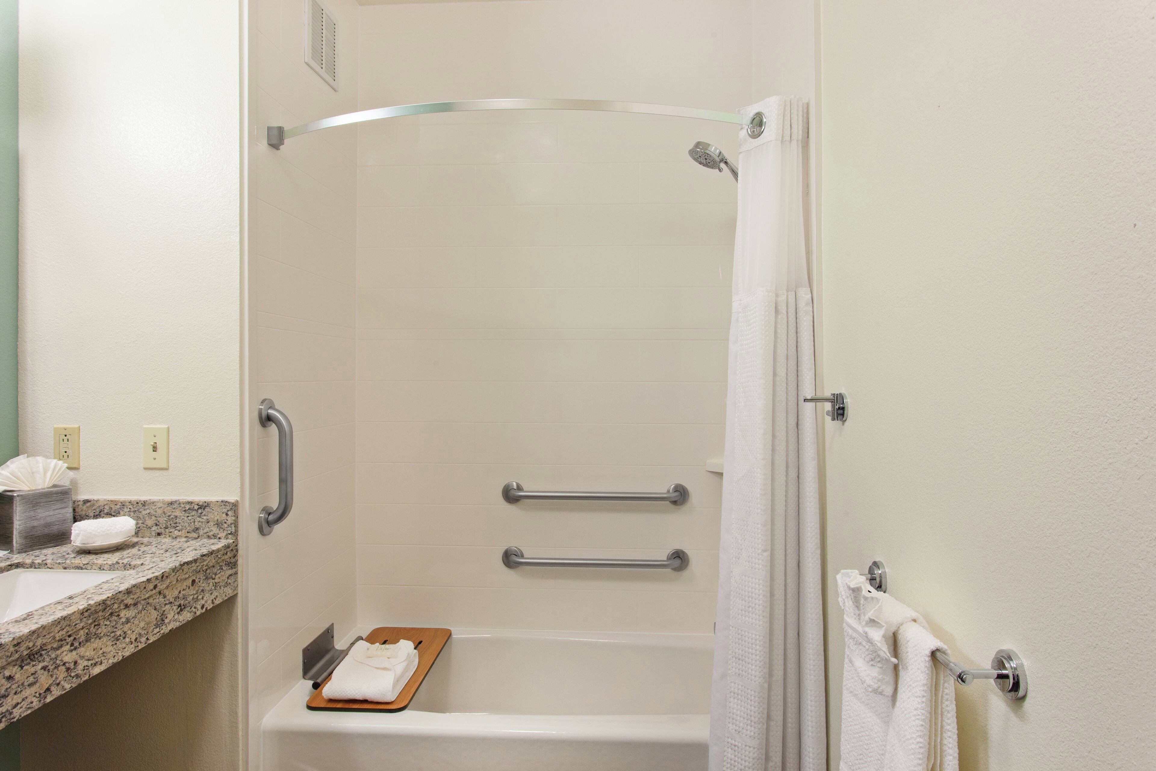 A bathroom with a shower, grab bars, a towel rack, and a marble countertop.