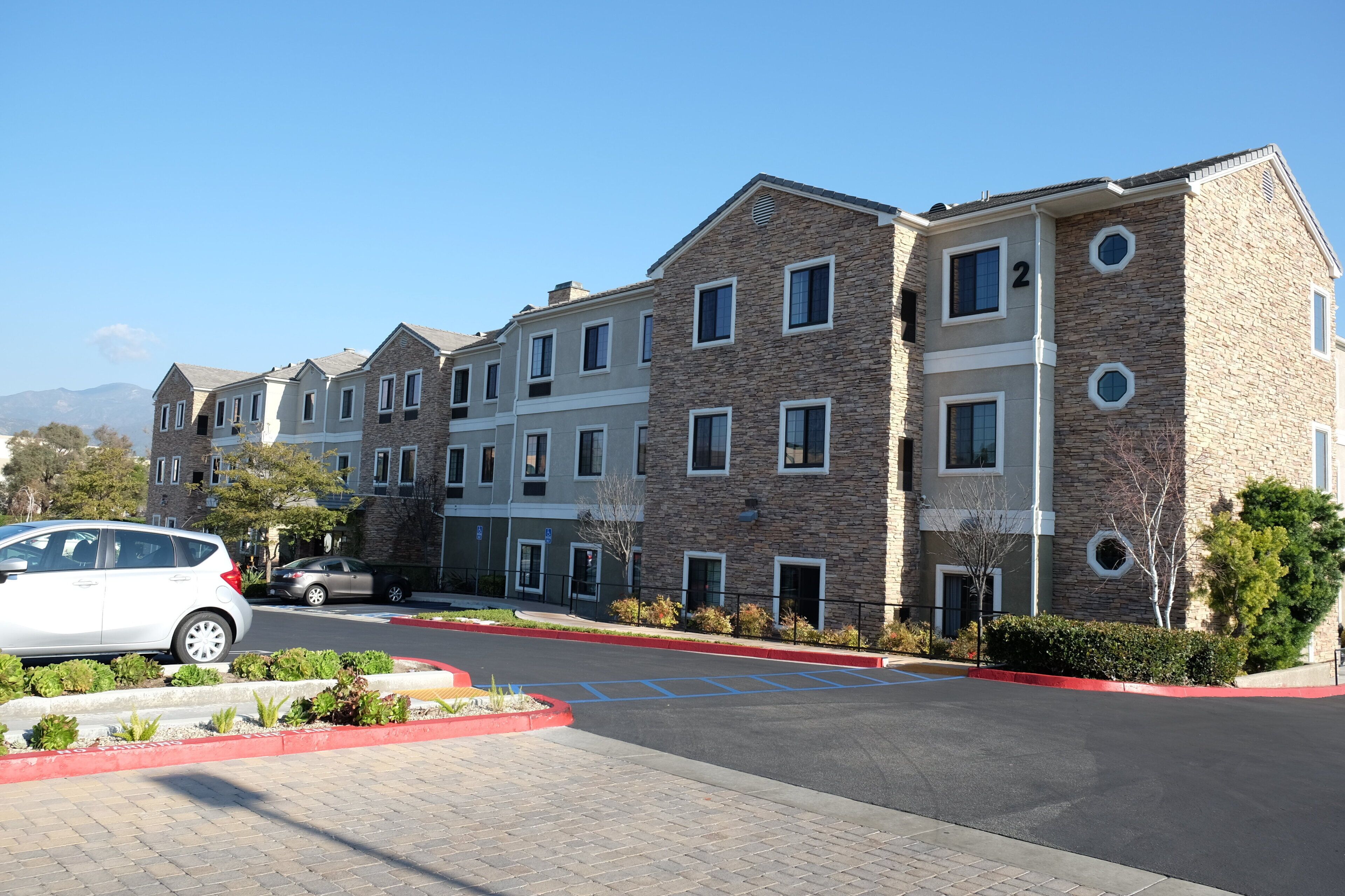 A multi-story residential building with a stone facade, multiple windows, and a parking area with a red curb.
