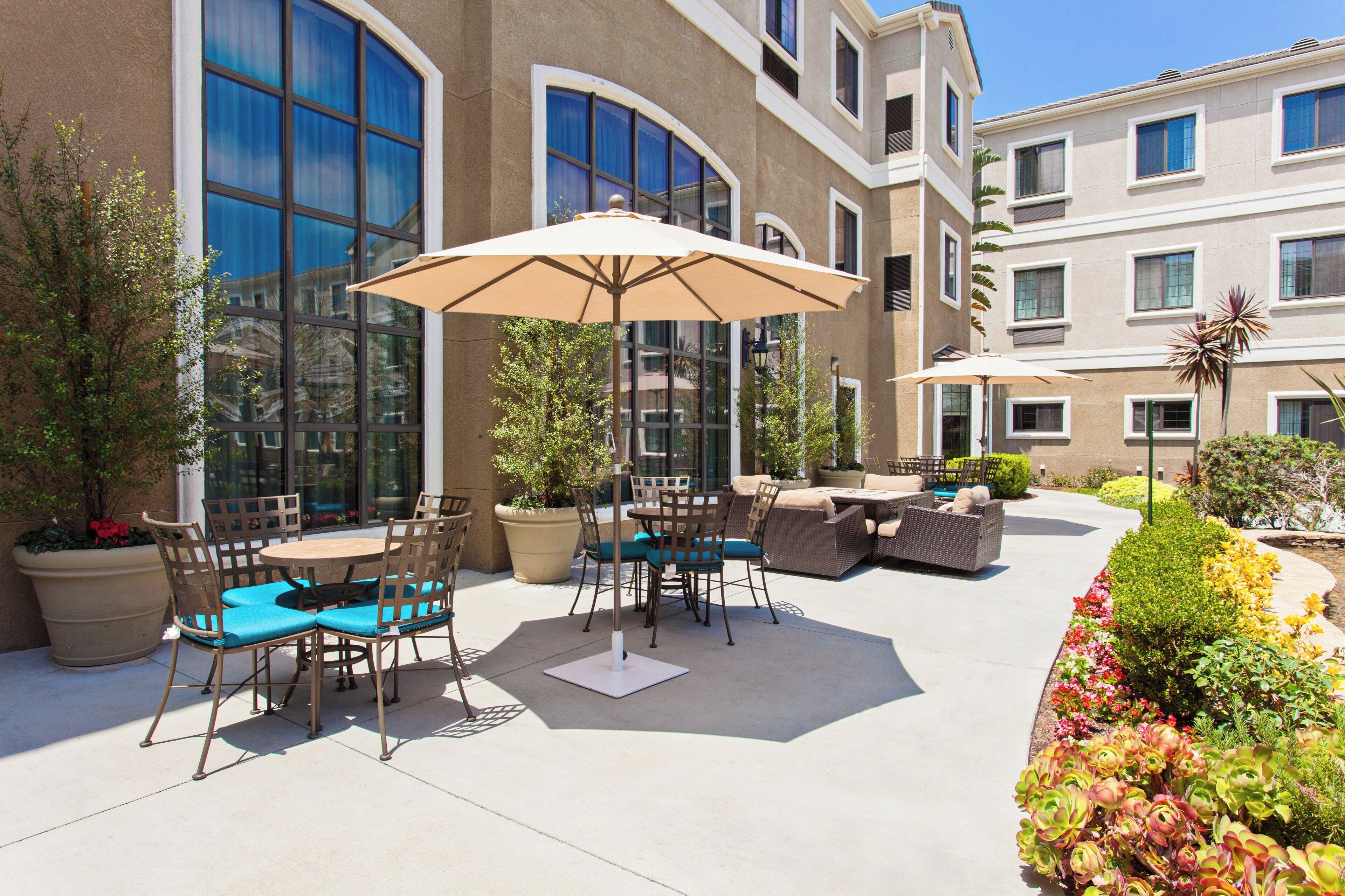 Un espace extérieur aménagé en terrasse, avec des tables et des chaises, un grand parasol et des plantes en pot.