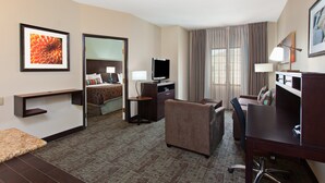 A hotel room with a bed, a desk, a chair, a television, and a desk lamp. - Staybridge Suites Lake Forest by IHG (Foothill Ranch)