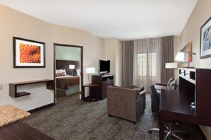 A hotel room with a bed, a desk, a chair, a television, and a desk lamp. - Staybridge Suites Lake Forest by IHG (Foothill Ranch)