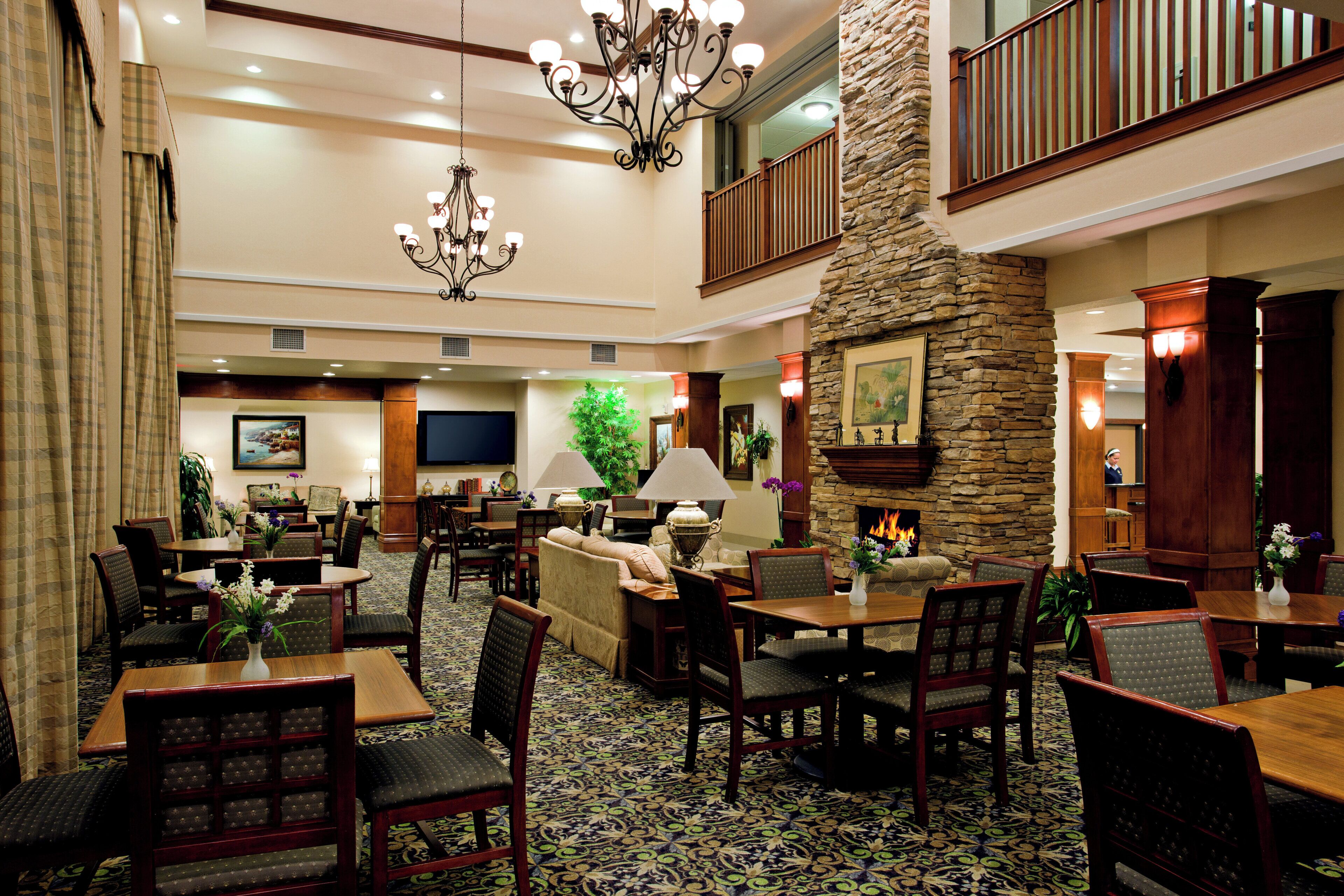A spacious lobby with a high ceiling, a stone fireplace, multiple seating areas, and a chandelier.