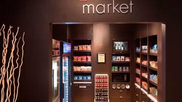 Interior de una tienda con estantes llenos de aperitivos, un expositor refrigerado y una máquina expendedora.